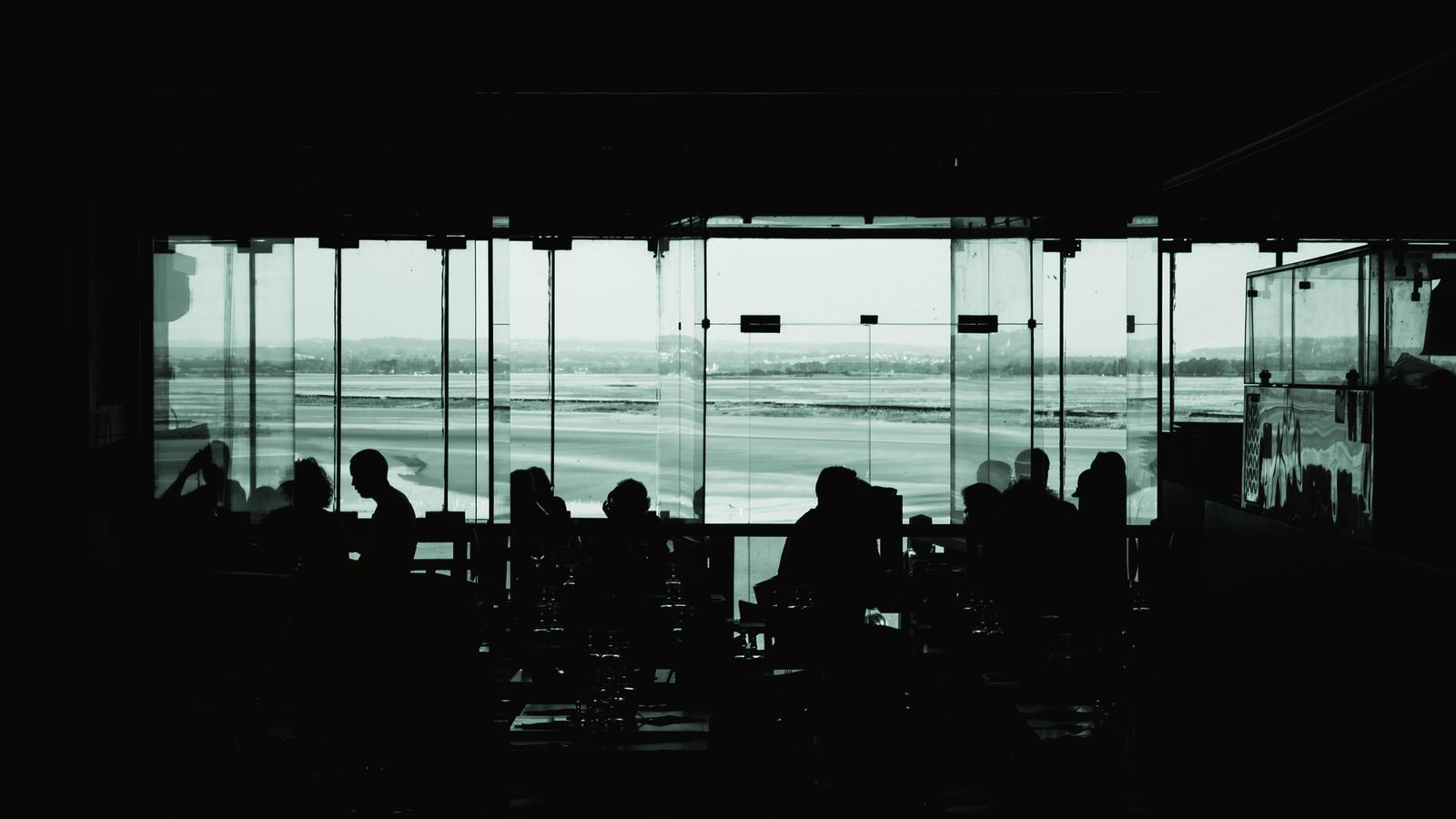 Travellers silhouetted against the glazing of a departure lounge, aircraft outside